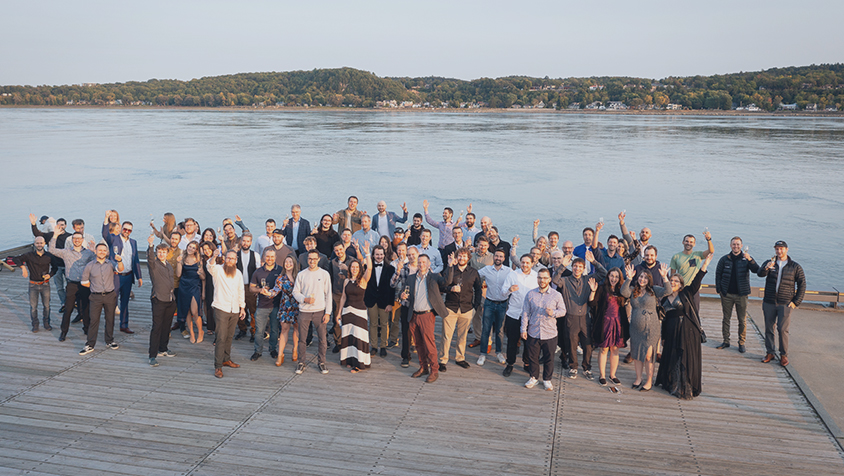 Photo de groupe de l’équipe Vooban, bras levés, sur un quai au bord d’un fleuve