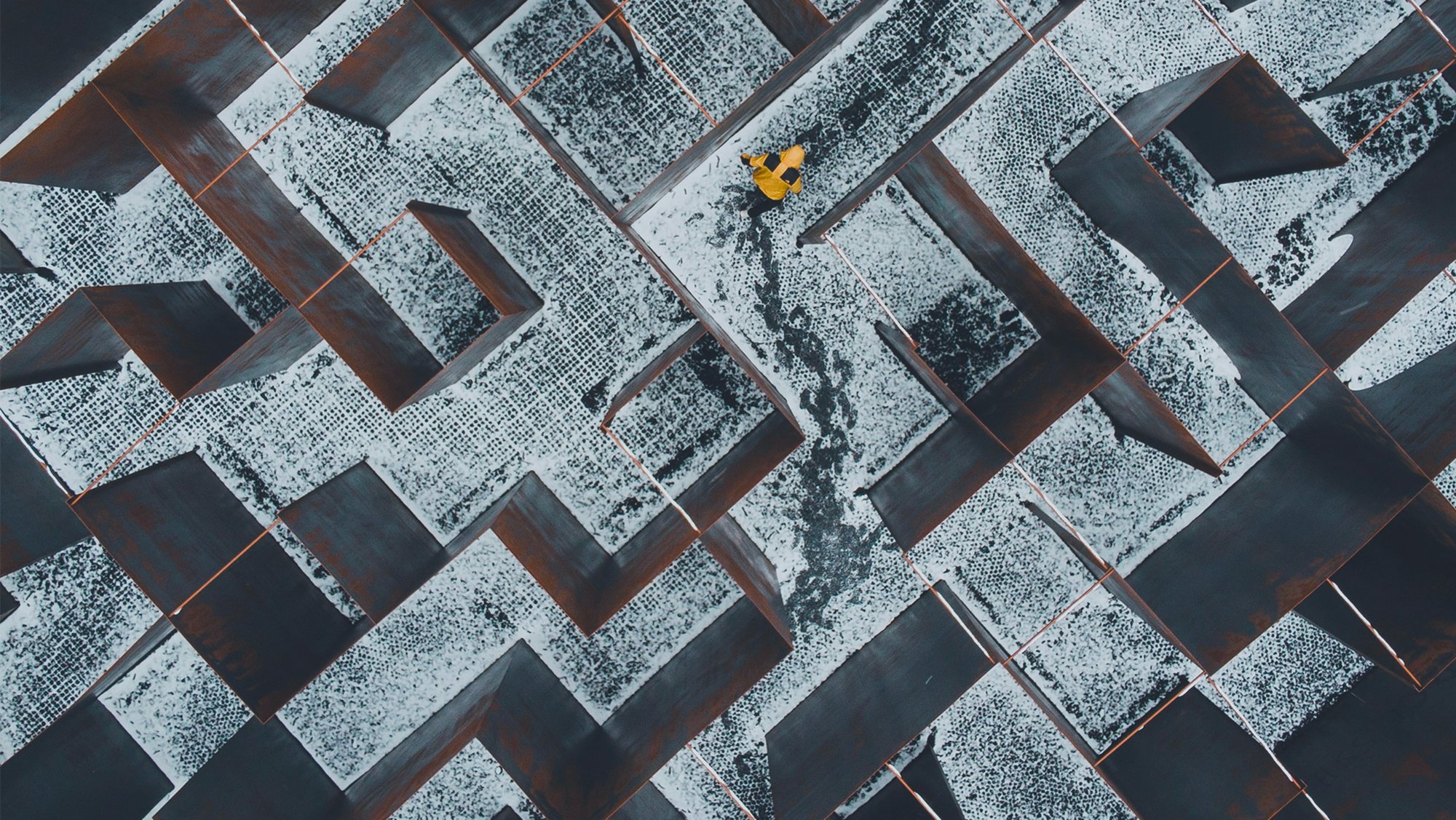 Aerial view of a person in a yellow coat in a maze of snowy metal walls