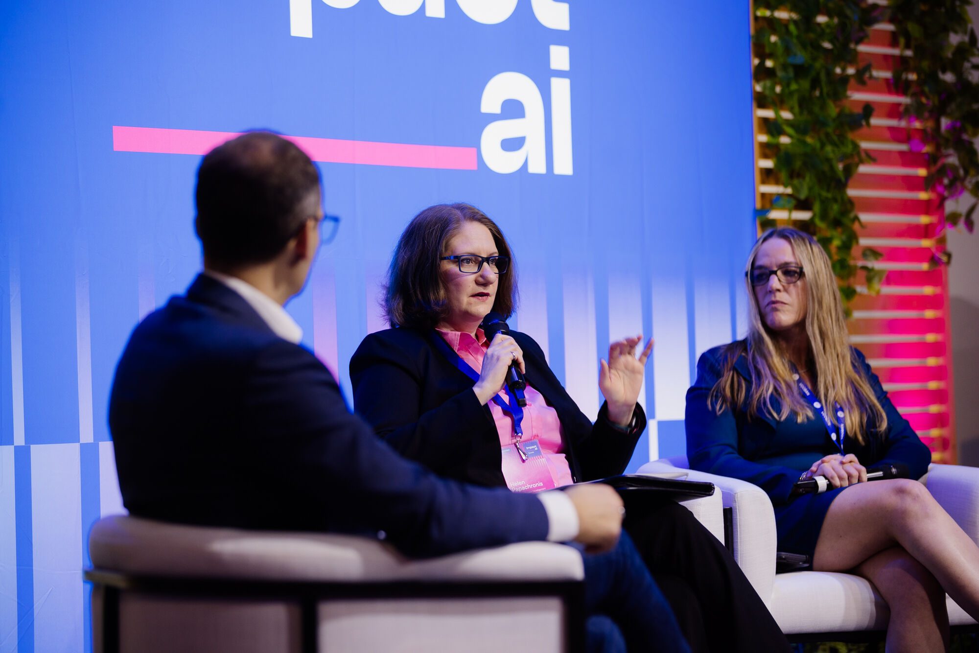 Helen Papachronis parle au micro entre un animateur vu de dos et une autre panéliste, à Impact AI