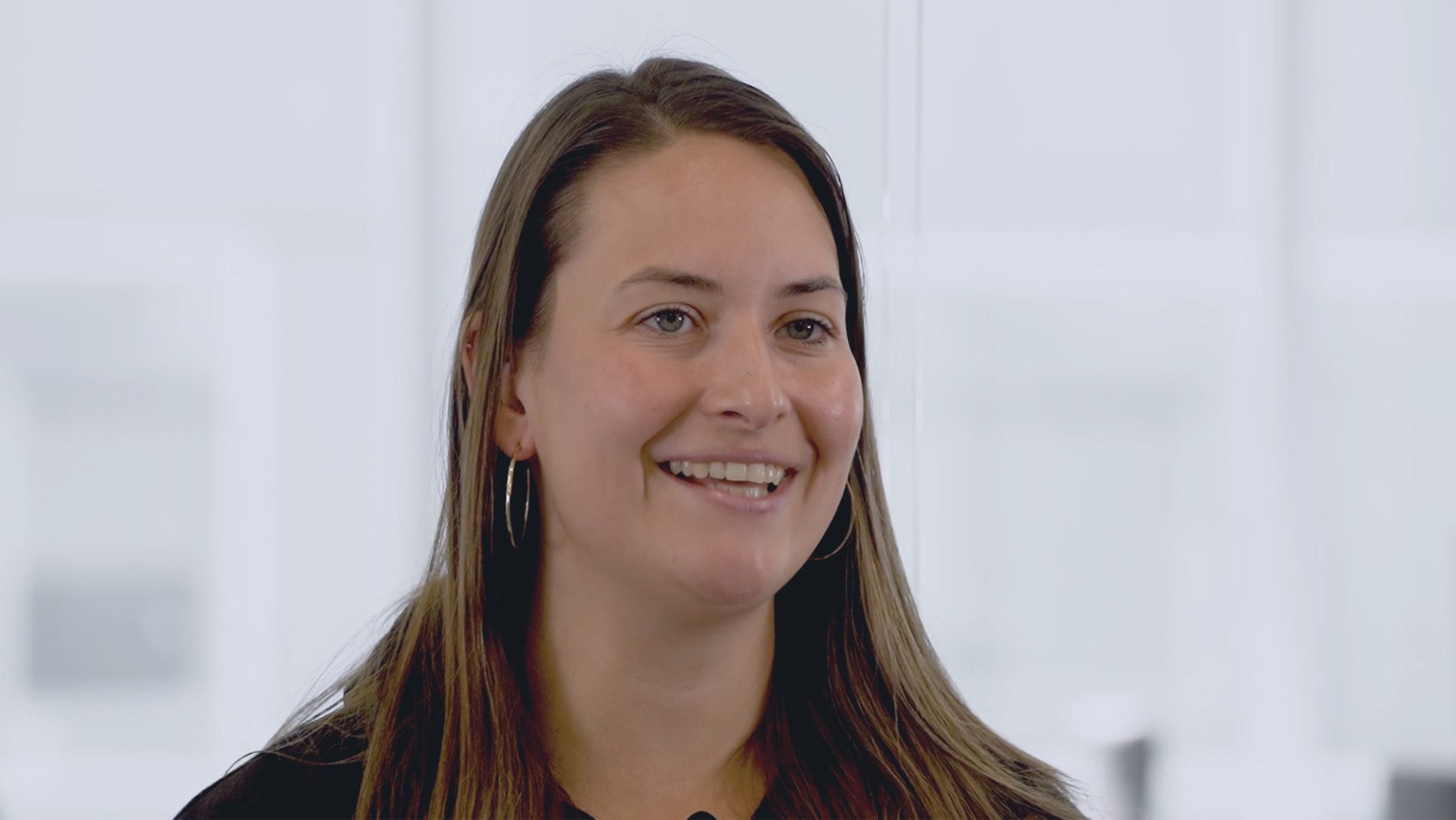 Close-up of a smiling woman with long hair in a bright office