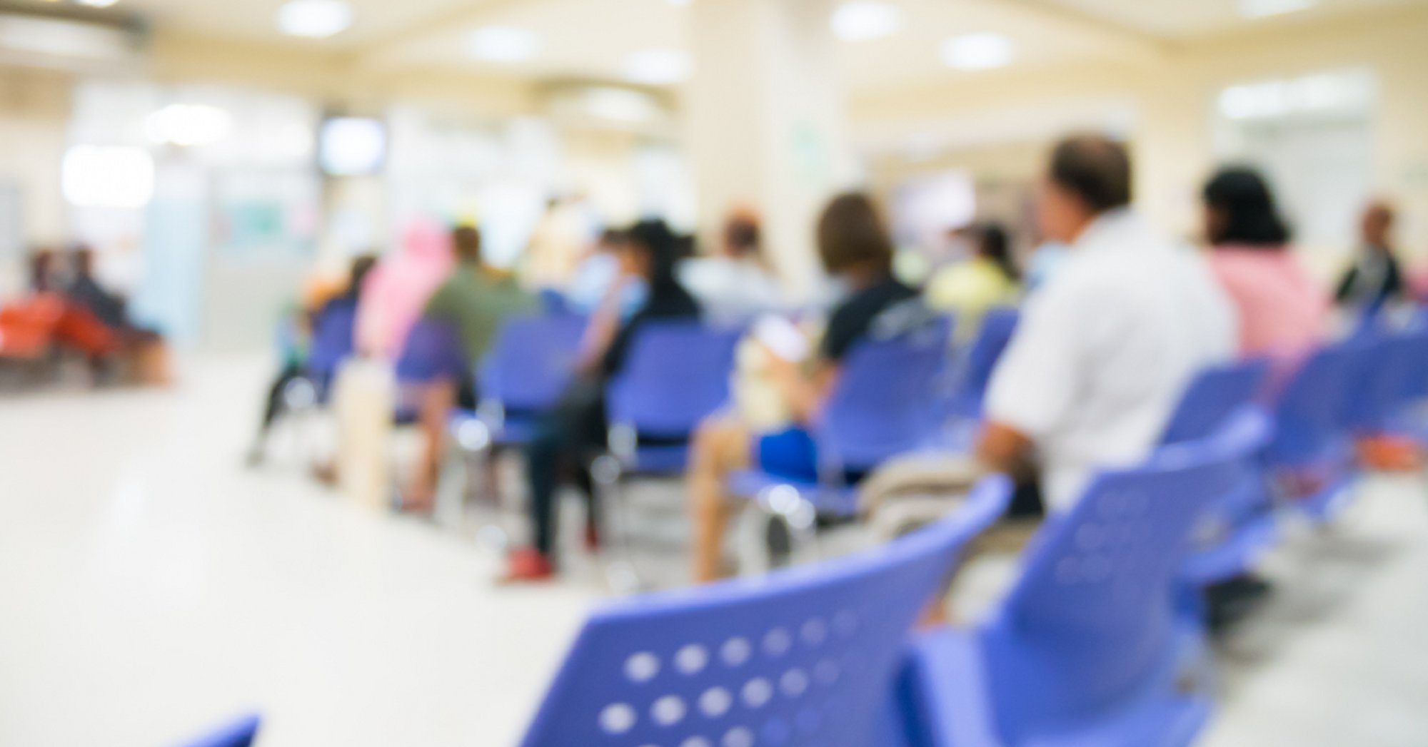 Blurred waiting room with people seated on blue chairs
