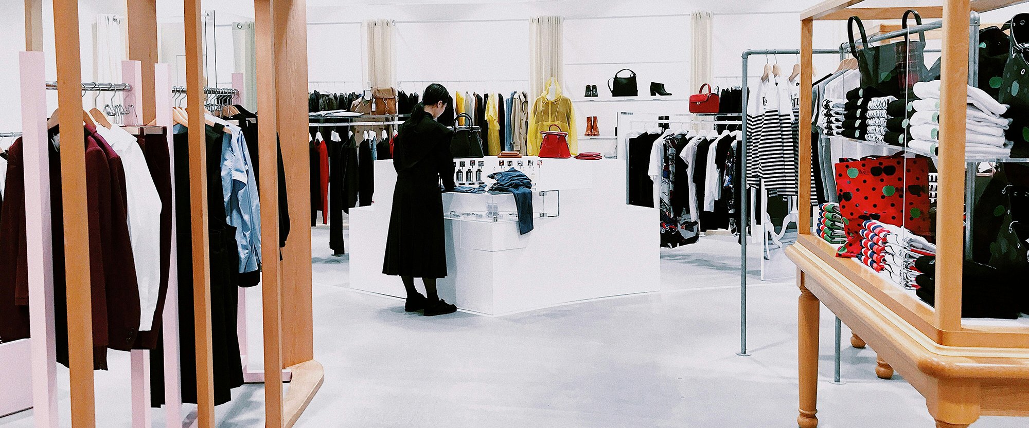 A shopper looks at clothes on a display table in a store with wooden racks