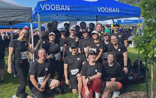 Team in black shirts with race bibs posing under a Vooban tent at a running event