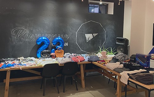 Tables covered with clothes in front of a “Bienvenue” chalkboard and blue balloons forming the number 22