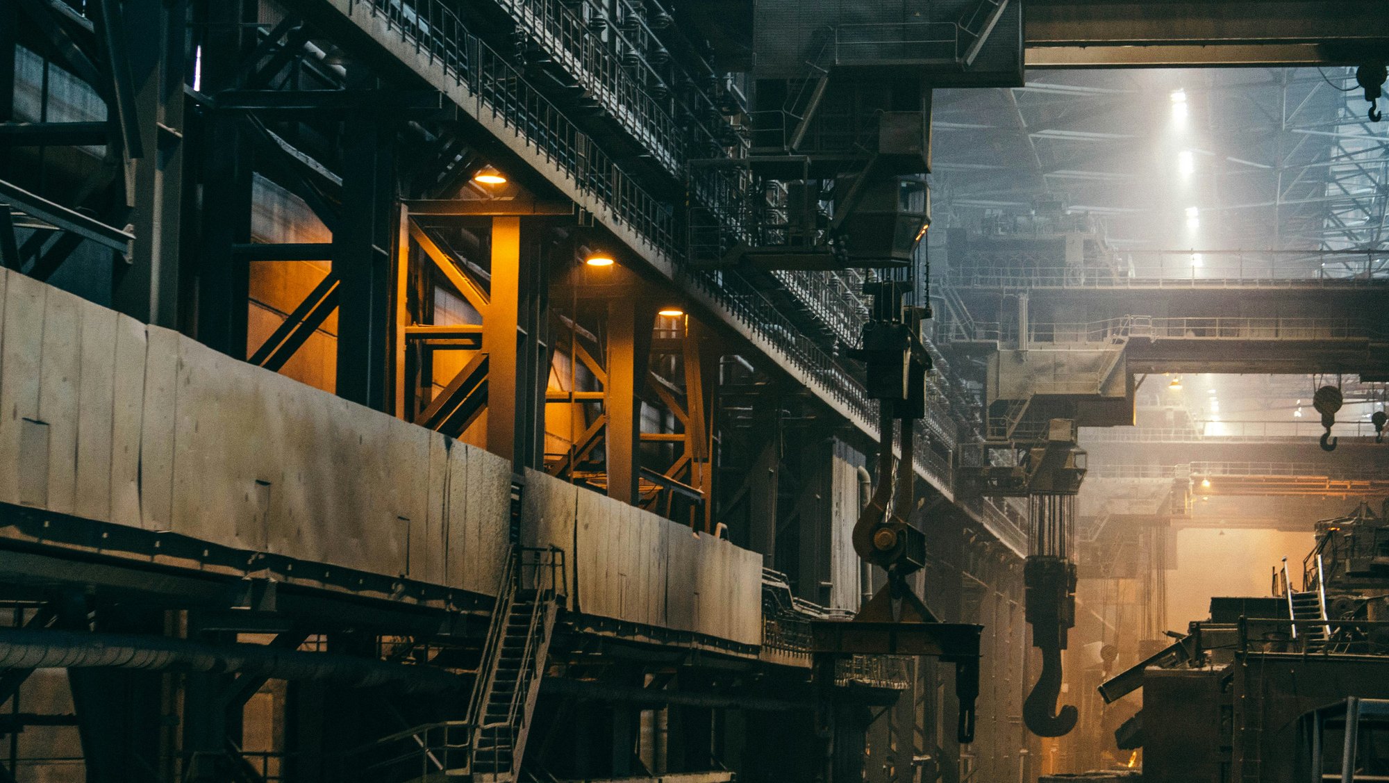 Dark interior of a steel plant with walkways, metal beams and overhead crane hooks