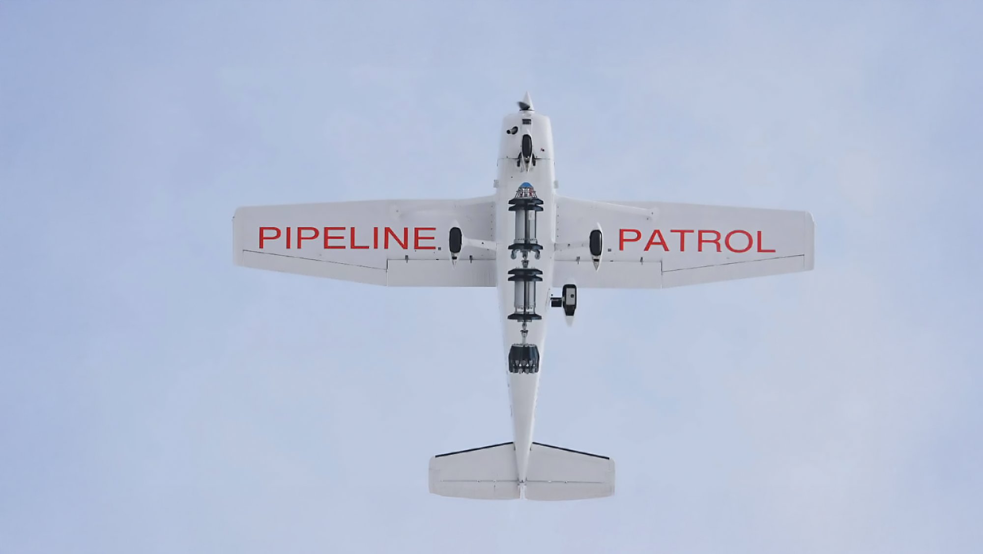 Petit avion vu de dessous, équipements fixés sous le fuselage, avec l’inscription « Pipeline Patrol » sur les ailes
