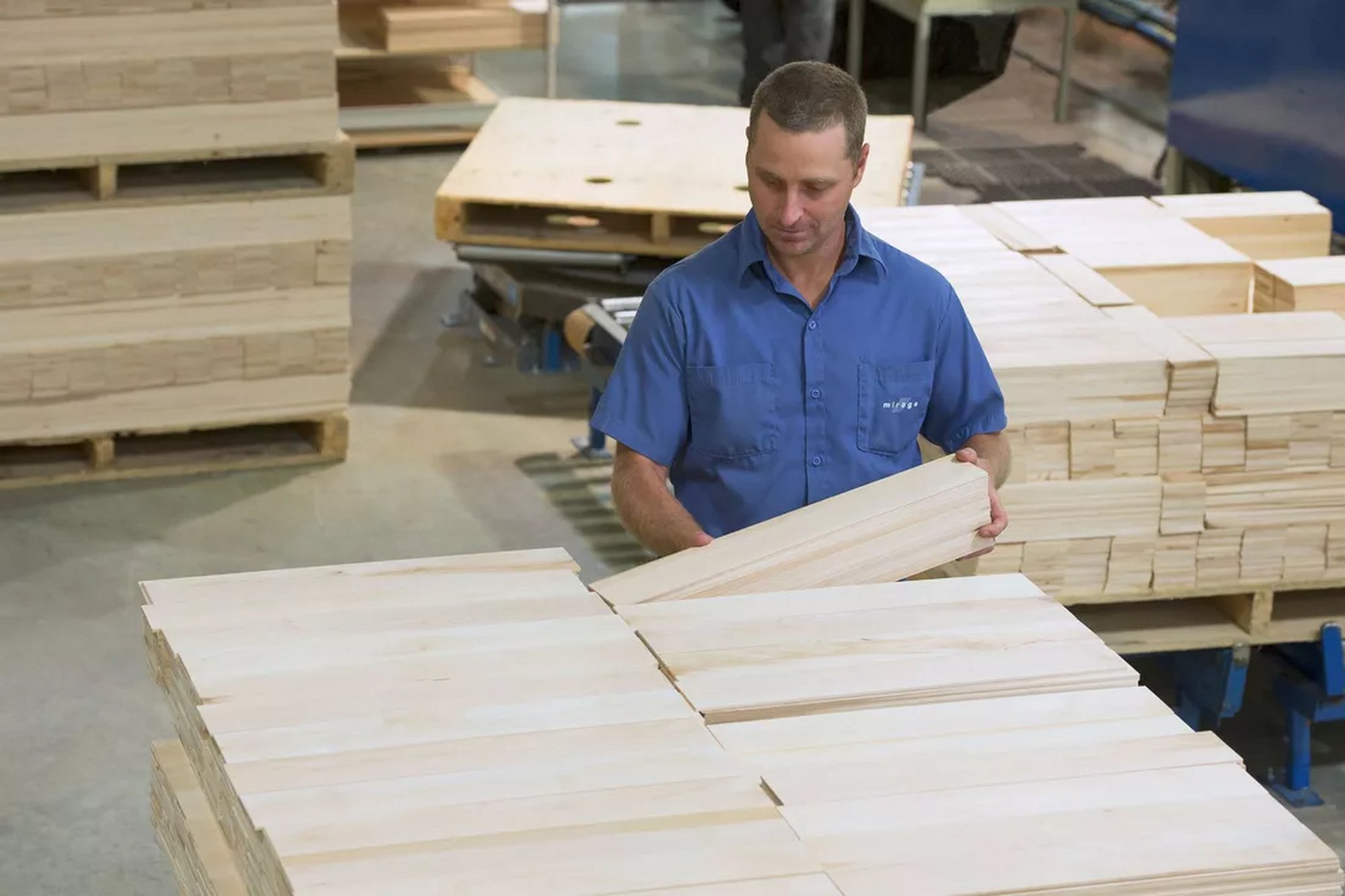 Mirage employee in a blue shirt handling hardwood boards in the plant